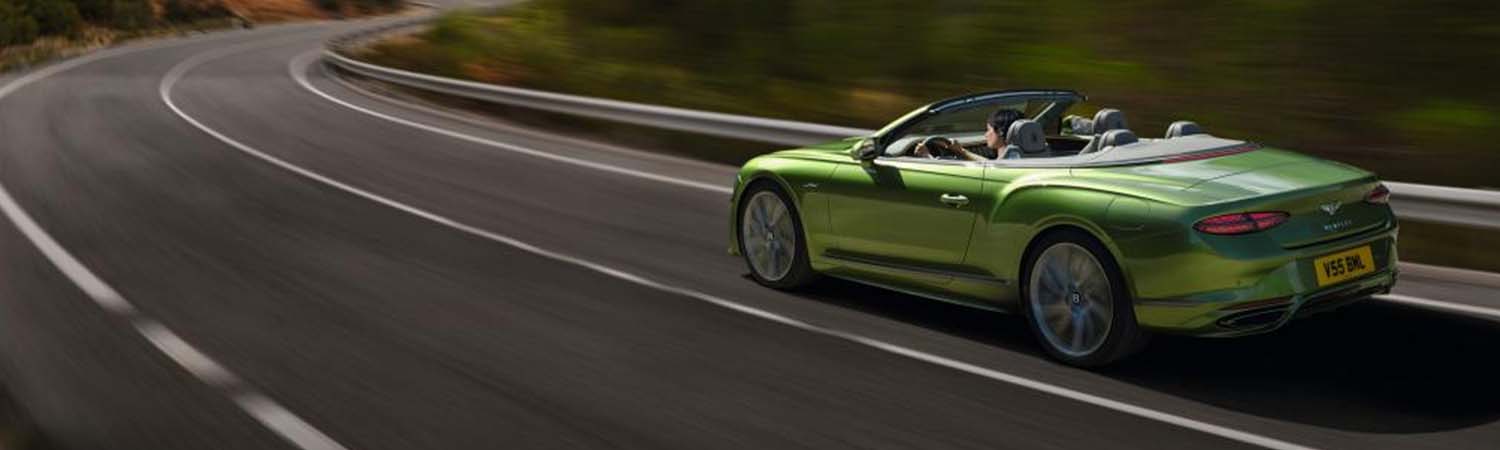 Exterior shot of a Bentley Continental GT Convertible driving on a highway.