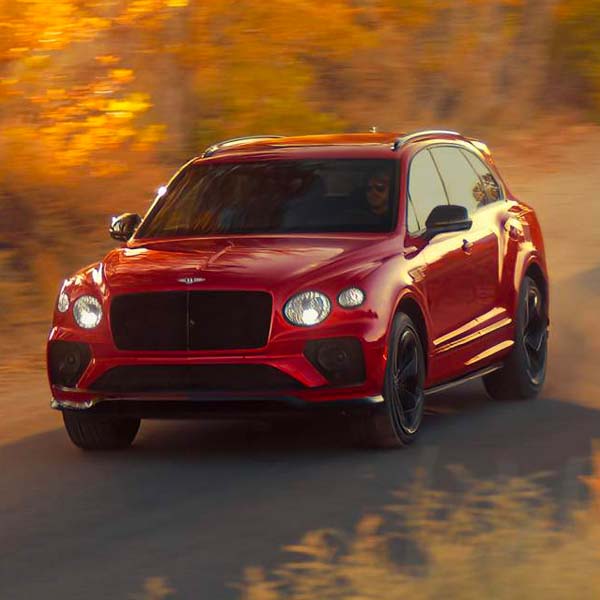 2024 Bentley Bentayga S driving on a road with trees in the background.